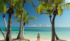 a man standing next to a palm tree on a beach