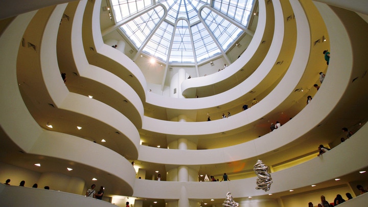 a large clock hanging from the ceiling with Solomon R. Guggenheim Museum in the background