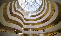 a large clock hanging from the ceiling with Solomon R. Guggenheim Museum in the background