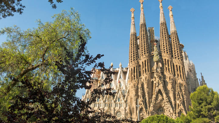 a large tall tower with a sky background with Sagrada Família in the background