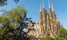 a large tall tower with a sky background with Sagrada Família in the background